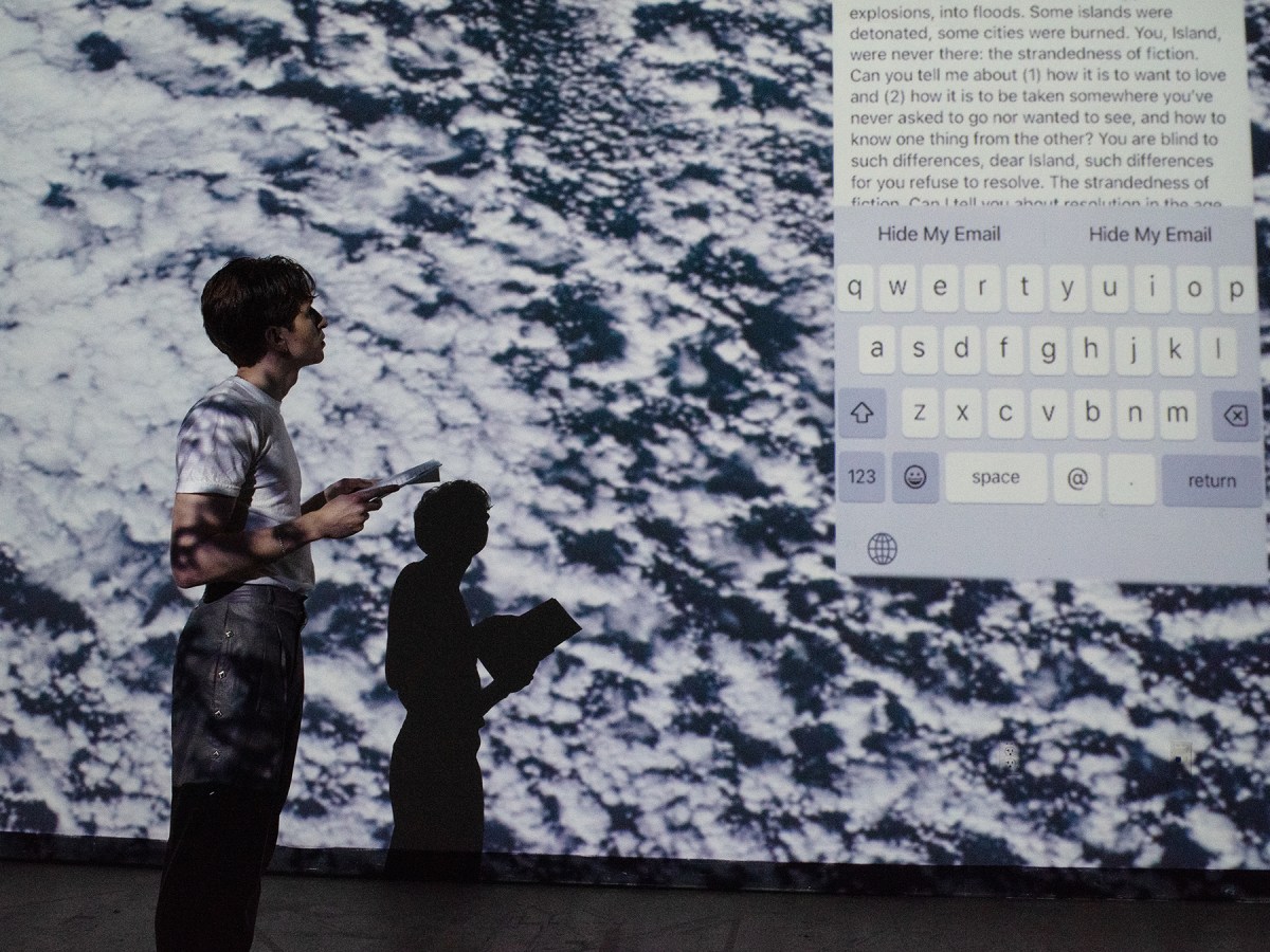 Drew Zeiba Bard MFA Writing class of 2024 performing their work “The Mirror”. Drew is reading in front of a black-and-white projection and a screenshot of an email on a smartphone screen.